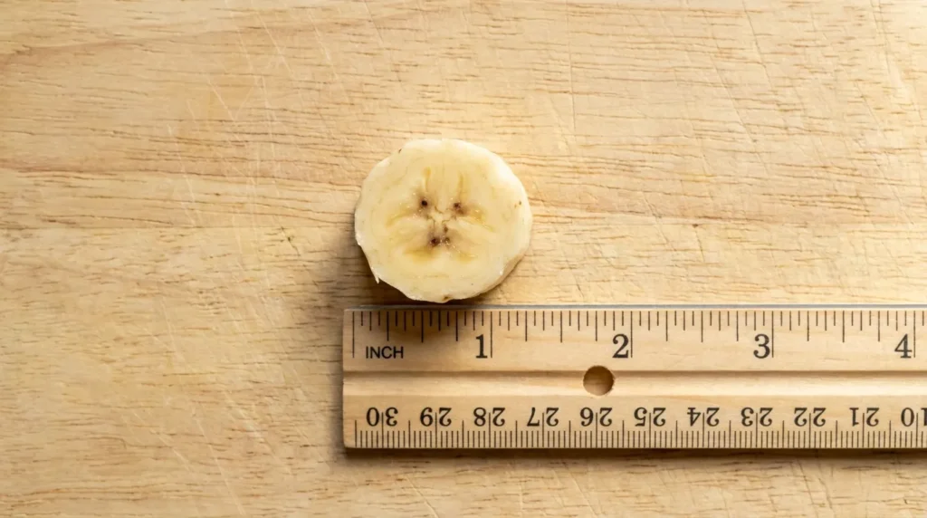 A 1-inch piece of banana next to a ruler on a wooden board showing safe cat serving size